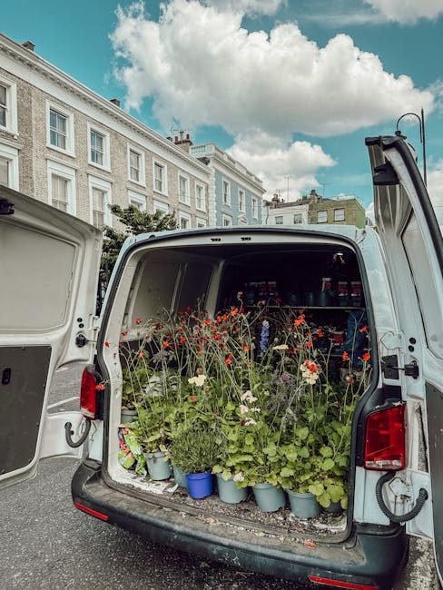 A photo of the open rear of a white delivery van parked on a street with historical white terraced buildings and a partly cloudy sky in the background. The van's cargo area is filled with a variety of