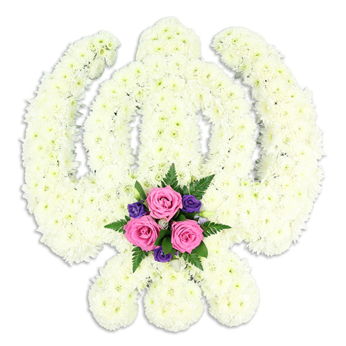 A large, reverent floral arrangement in the shape of the Sikh Khanda symbol takes centre stage, composed almost entirely of densely packed white chrysanthemums and framed by a pure white studio background. The emblem's structure is immediately recognisable: a straight, double-edged sword standing upright at the core; a flawless circular chakkar encircling it; and two curved kirpans extending outward and downward to form a balanced, symmetrical silhouette. Each element is defined by compact cushions of chrysanthemum blooms, placed meticulously so that the surface looks smooth yet richly textured, like a soft tapestry of white and cream petals. The blooms' natural variation in tone creates quiet interest, while the overall impression remains one of purity and calm. At the very bottom of the design, resting between the lower tips of the kirpans, a contrasting cluster of accent flowers softens the formality. Three pink roses, their petals gently unfurling, sit together like a small, tender heart within the tribute. Surrounding them, deep purple flowers add a thoughtful, solemn depth of colour, while wisps of green fern and polished foliage thread through the cluster, echoing the greenery found around South Hackney's residential squares and tree-lined streets near London Fields and Mare Street. A soft, diffused shadow beneath the arrangement provides a sense of three-dimensional presence without disturbing the tranquillity of the scene. Created by Florist South Hackney with an understanding of Sikh customs and local families, this floral Khanda is the kind of piece chosen to honour a loved one at a funeral, memorial service, or spiritual gathering, symbolising courage, unity, and enduring remembrance.