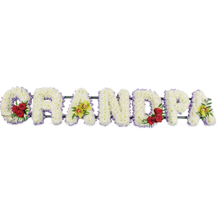 The floral arrangement portrayed here is a horizontal funeral tribute spelling "GRANDPA," rendered in bold yet gentle letters made entirely from white chrysanthemums. Each letter is full and rounded, composed of densely packed chrysanthemum heads that form a soft, cushion-like texture, evoking a sense of comfort and calm. The arrangement is photographed against a bright white background, which heightens the contrast with the flowers and allows viewers to see every curve and contour of the lettering. Bordering each letter is a slim band of lavender-purple ribbon, a delicate outline that adds a whisper of colour and helps the shapes stand clearly apart. Within the sweeping curve of the initial "G" rests a neat cluster of three or four deep red roses, framed by short sprigs of glossy green foliage, creating a rich, emotive note at the start of the word. The first "A" in the sequence carries several yellow-green orchid blooms, their elegant forms and subtle reddish shading introducing a sophisticated, slightly exotic accent. Echoing this theme, the inner curve of the "D" contains another small group of red roses and greenery, while the final "A" repeats the luminous yellow-green orchids, bringing visual balance and a sense of completion. Slender metal support bars are faintly visible behind the flowers, holding each letter in perfect alignment so the tribute can be displayed with confidence at South Hackney funerals, whether near the Regent's Canal or around the quiet streets off Victoria Park Road. The interplay of pure white, deep red, and tender orchid green conveys sorrow and affection in equal measure, honouring the memory of a dearly loved grandfather.